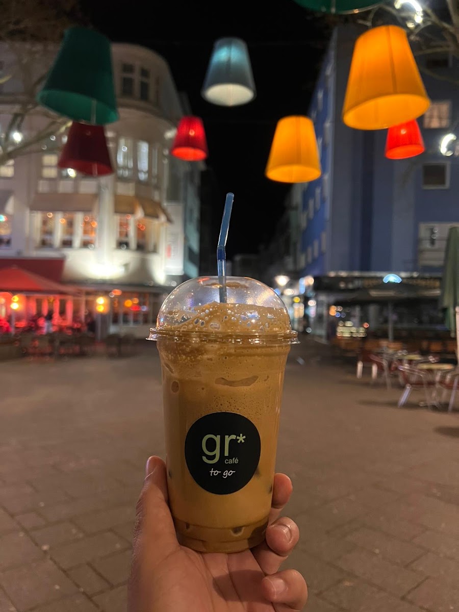 Café GR to-go Becher vor dem Lokal bei Nacht, mit den Lichterketten der Terrasse im Hintergrund